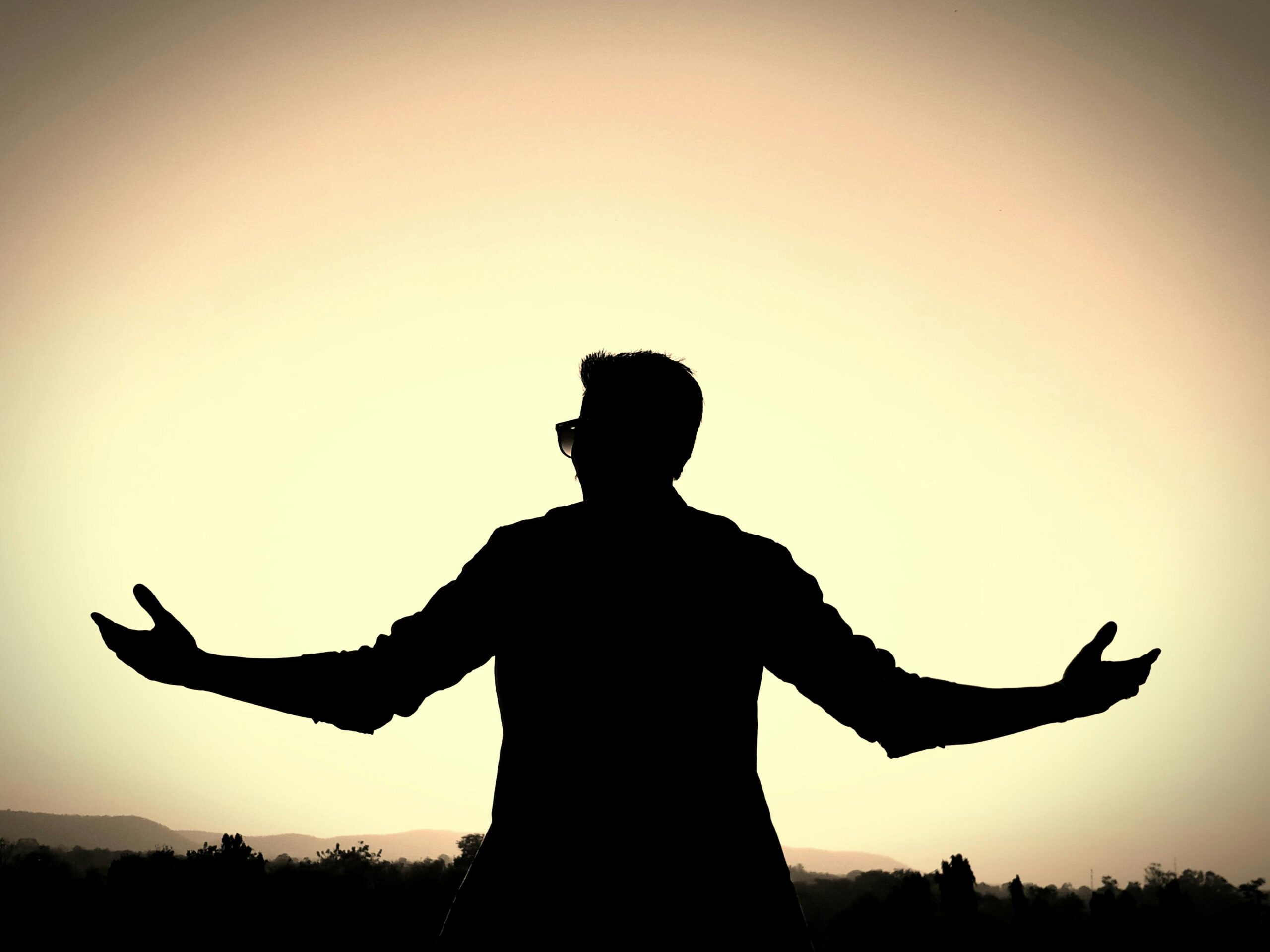 Silhouette of a man with open arms against a vibrant sunset background, symbolizing freedom and peace.